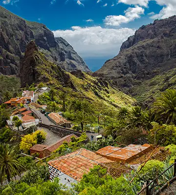 Pueblo con tejados rojos en valle verde entre monta&ntilde;as y cielo azul