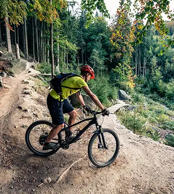 Ciclista de monta&ntilde;a pedalea por un camino de tierra entre bosques verdes