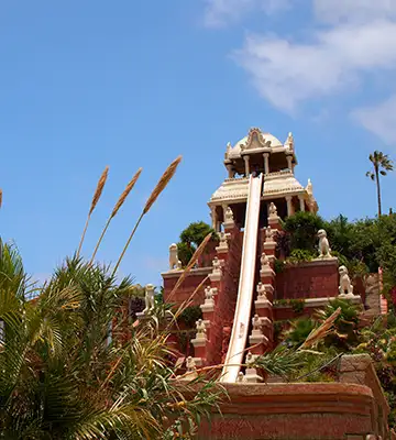 Torre hist&oacute;rica de piedra con plantas y cielo azul detr&aacute;s.