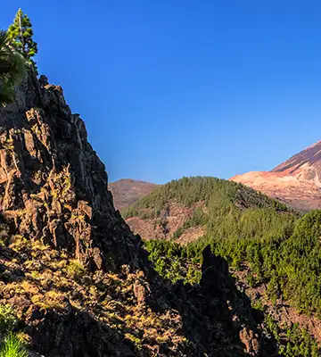 Monta&ntilde;as rocosas y valle verde bajo cielo azul despejado.