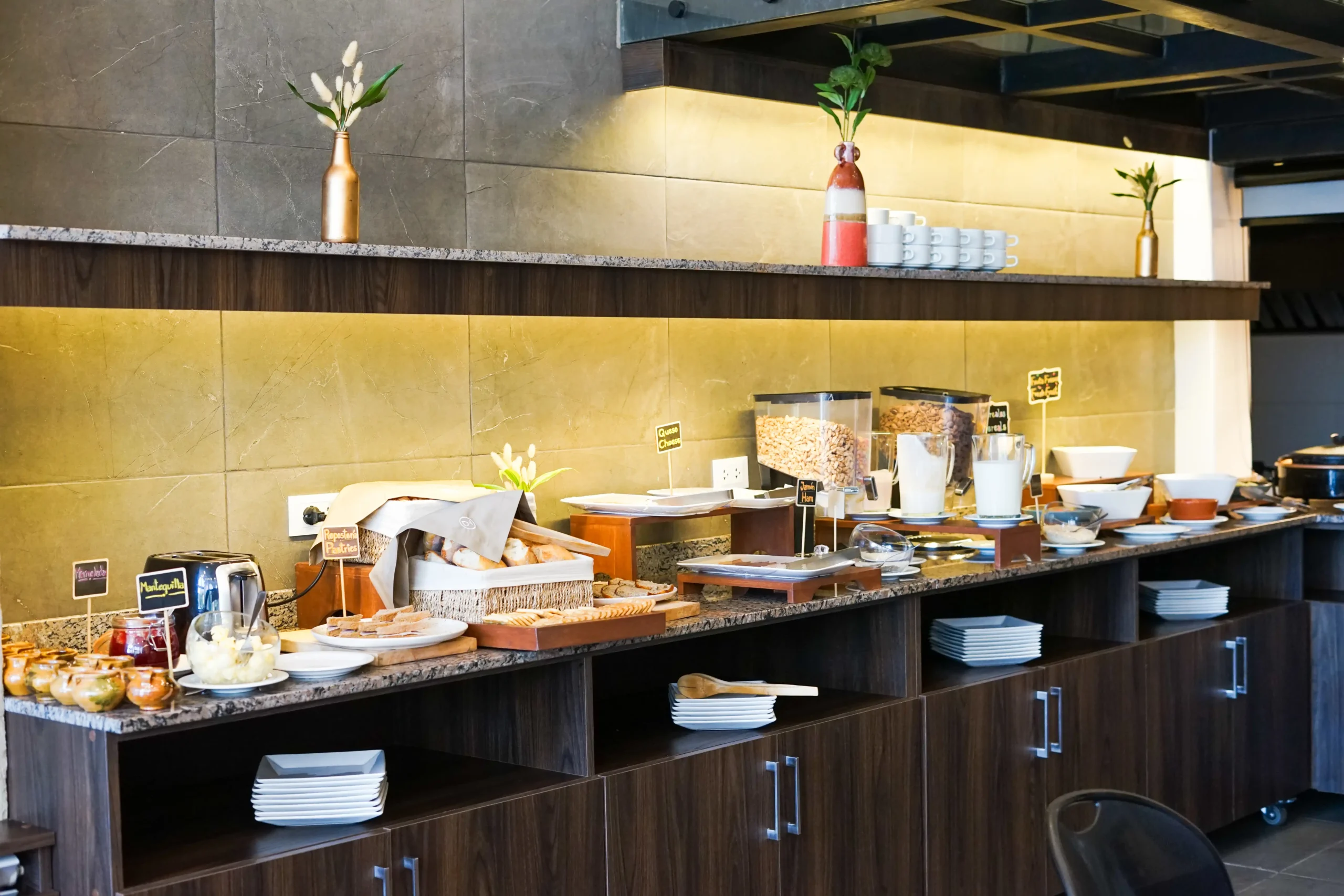 Buffet de desayuno con mesas, recipientes y plantas decorativas en la barra