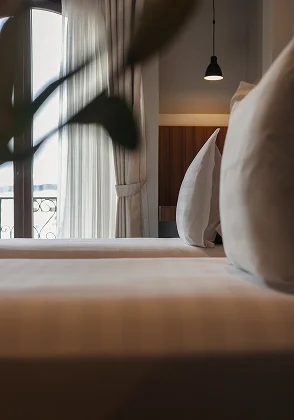 Cama con almohadas, luz c&aacute;lida y cortinas en una habitaci&oacute;n hotelera.