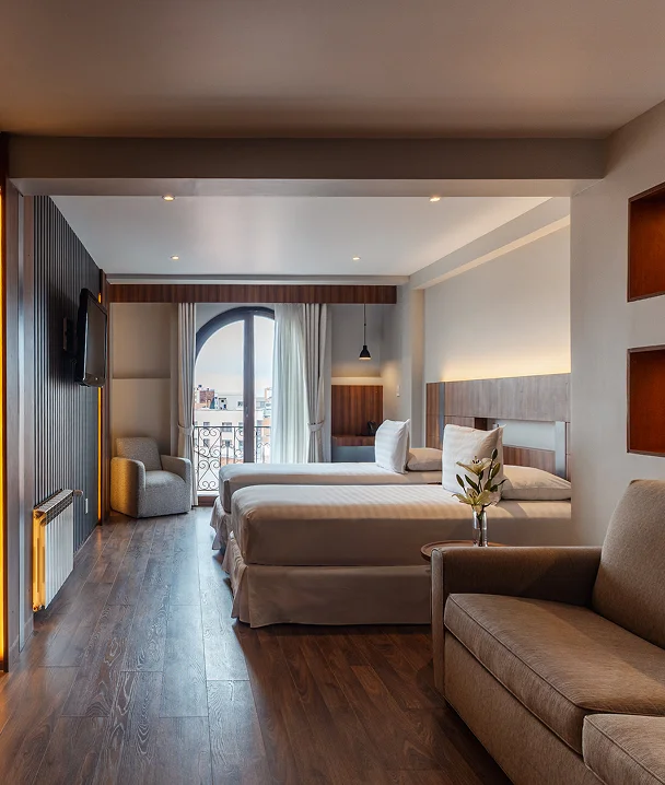 Interior de hotel con cama doble, sill&oacute;n y balc&oacute;n con arco.