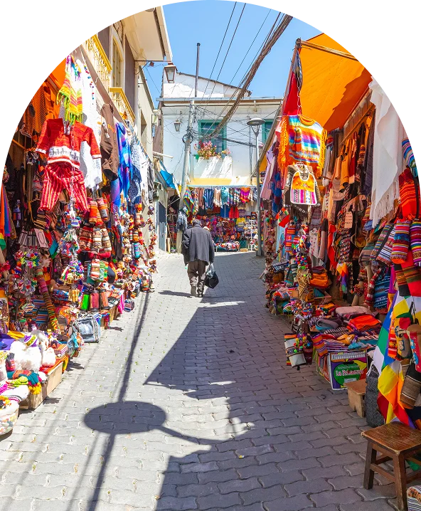 Calle estrecha con puestos de artesan&iacute;as y colores, y un peat&oacute;n al fondo
