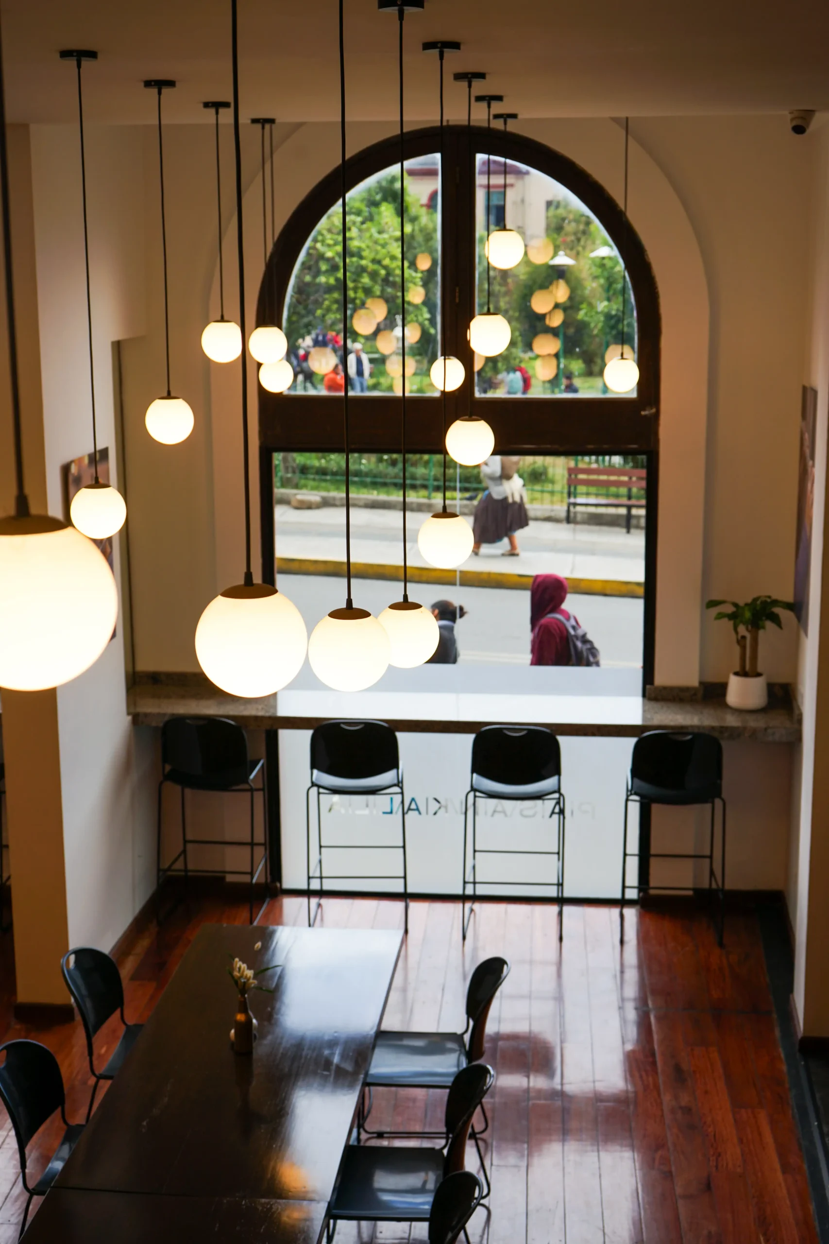 Interior de cafeter&iacute;a con l&aacute;mparas colgantes y vista al jard&iacute;n por un arco de vidrio
