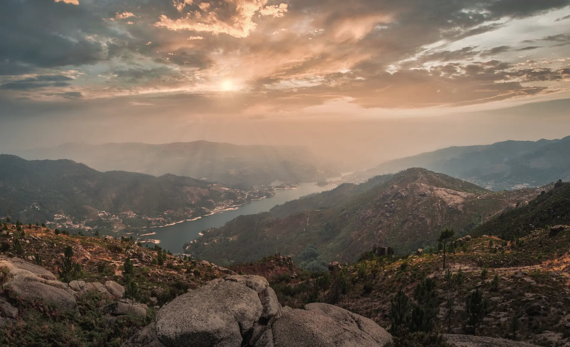 Vale montanhoso com rio ao p&ocirc;r do sol e nuvens dram&aacute;ticas
