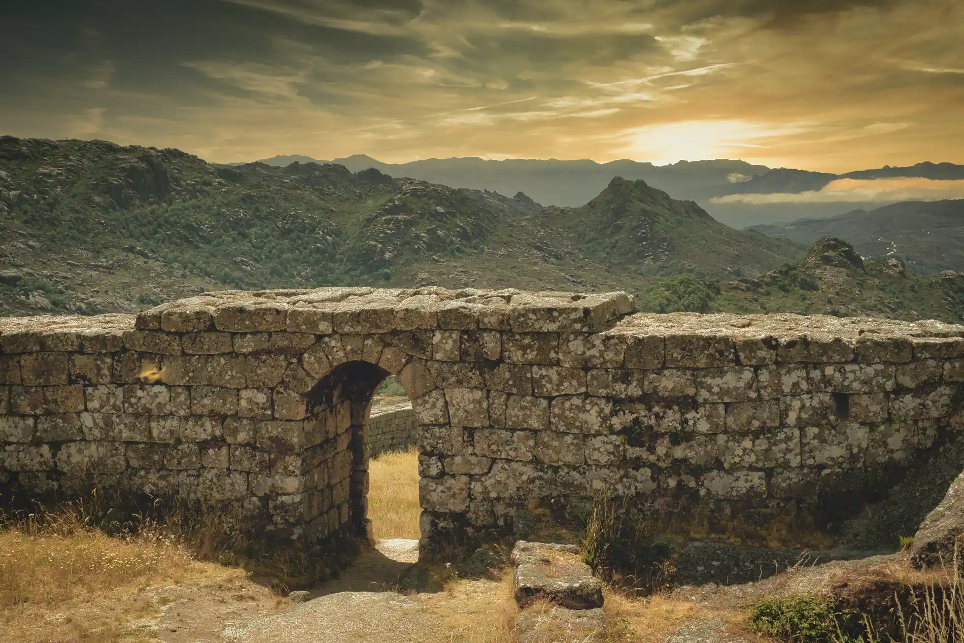 P&ocirc;r do sol nas montanhas com ru&iacute;nas de pedra em primeiro plano
