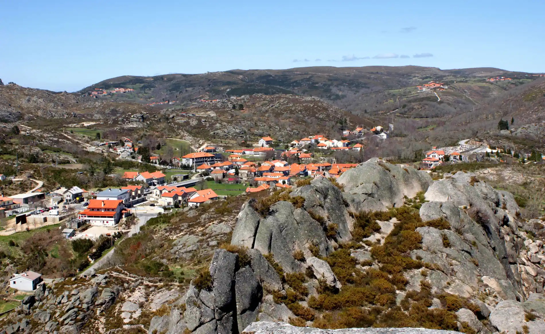 Vista de vila serrana com telhados laranja e montanhas ao fundo