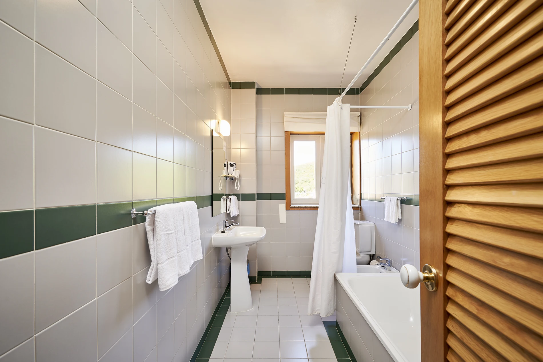 Banheiro moderno com azulejos claros, faixa verde, cortina e bancada branca