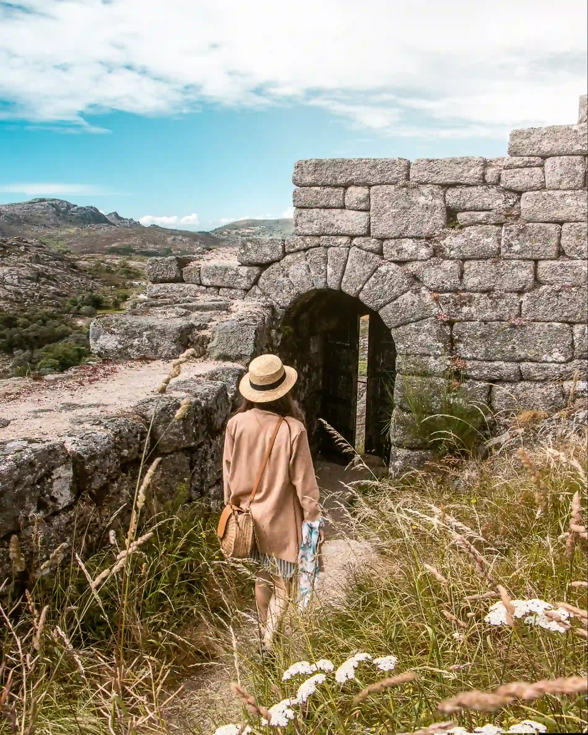 Turista de chapéu em frente a um túnel de pedra, montanhas ao fundo