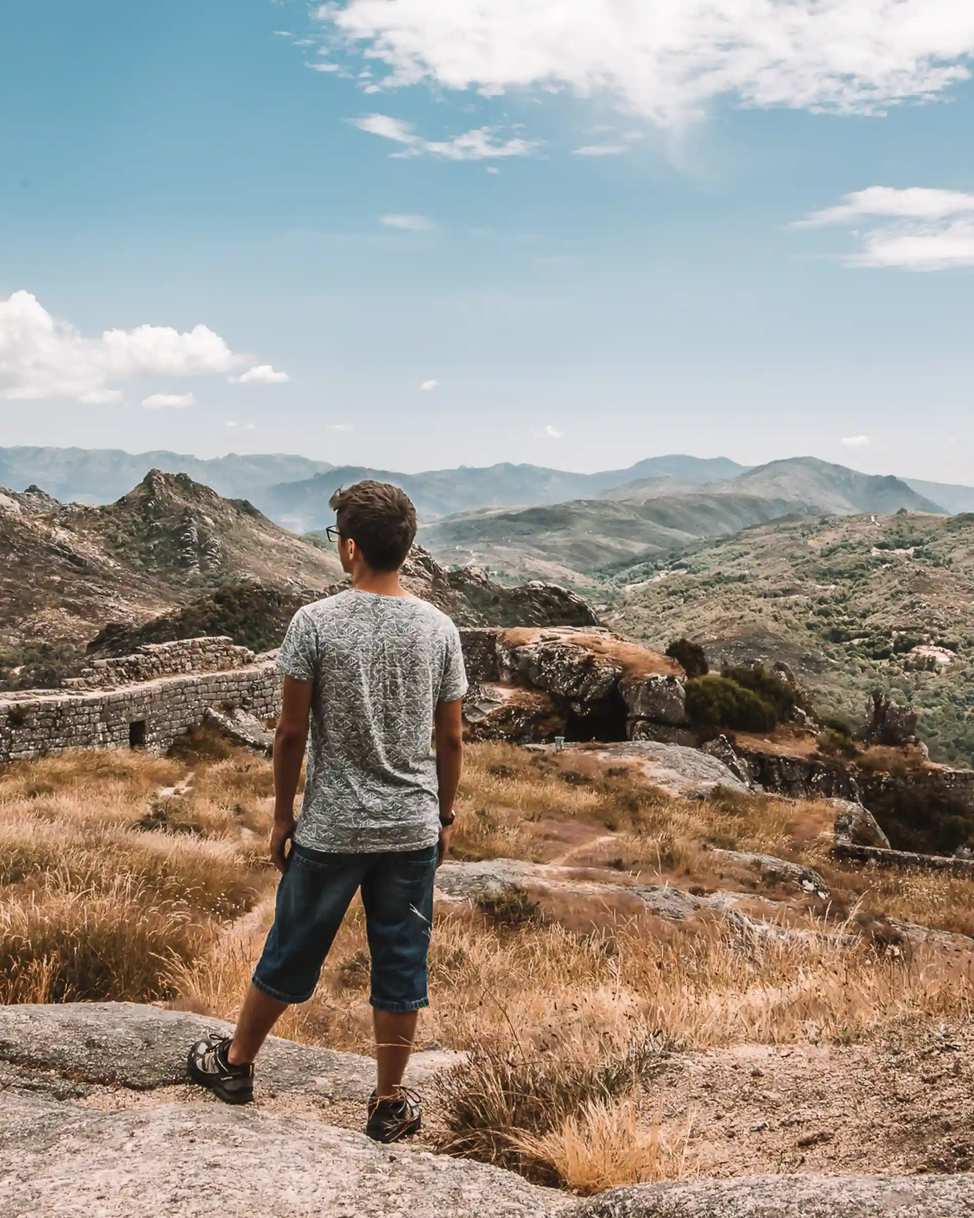 Homem de costas contempla montanhas e vale sob céu azul com nuvens