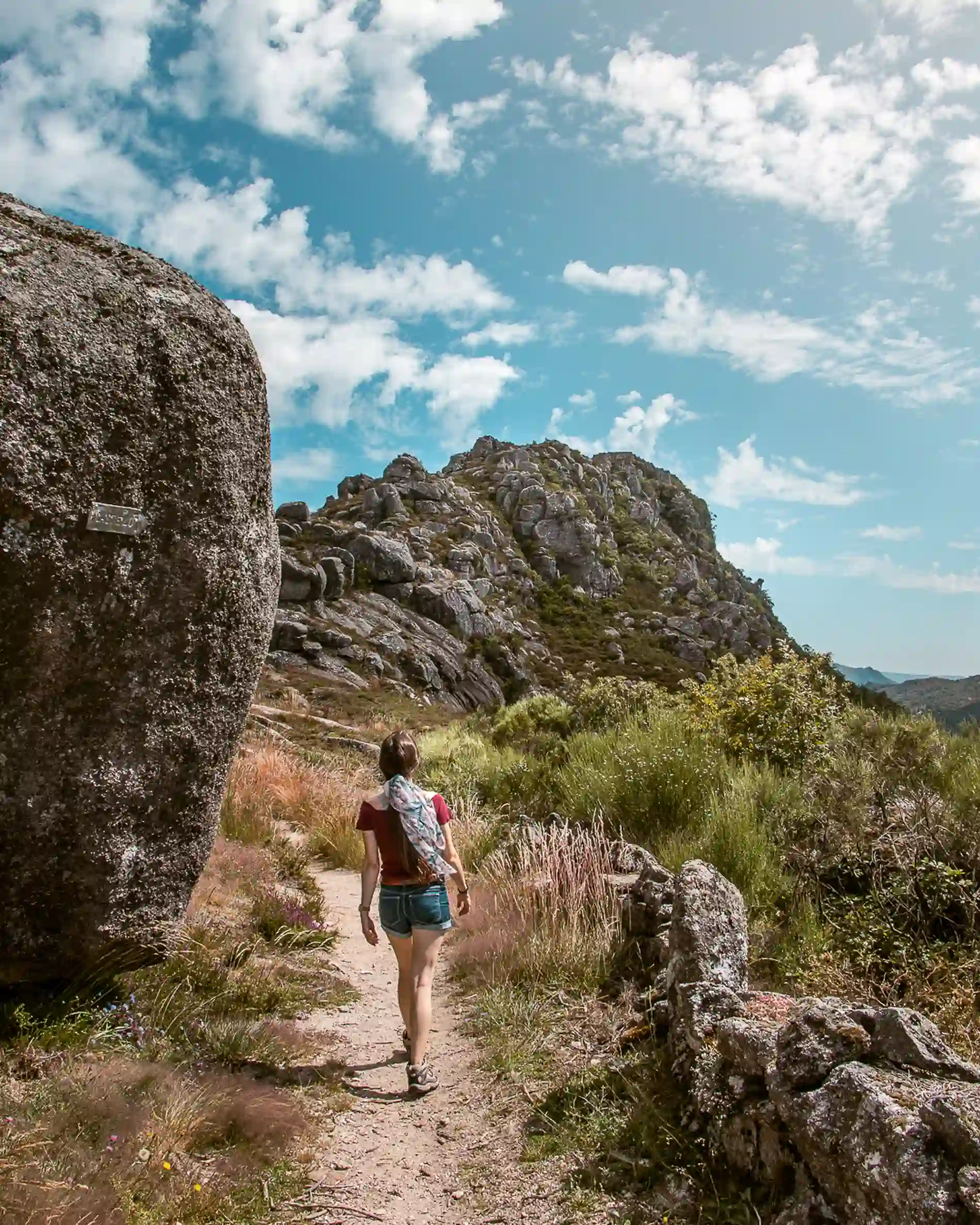 Caminhante trilha em montanhas rochosas sob céu azul e nuvens