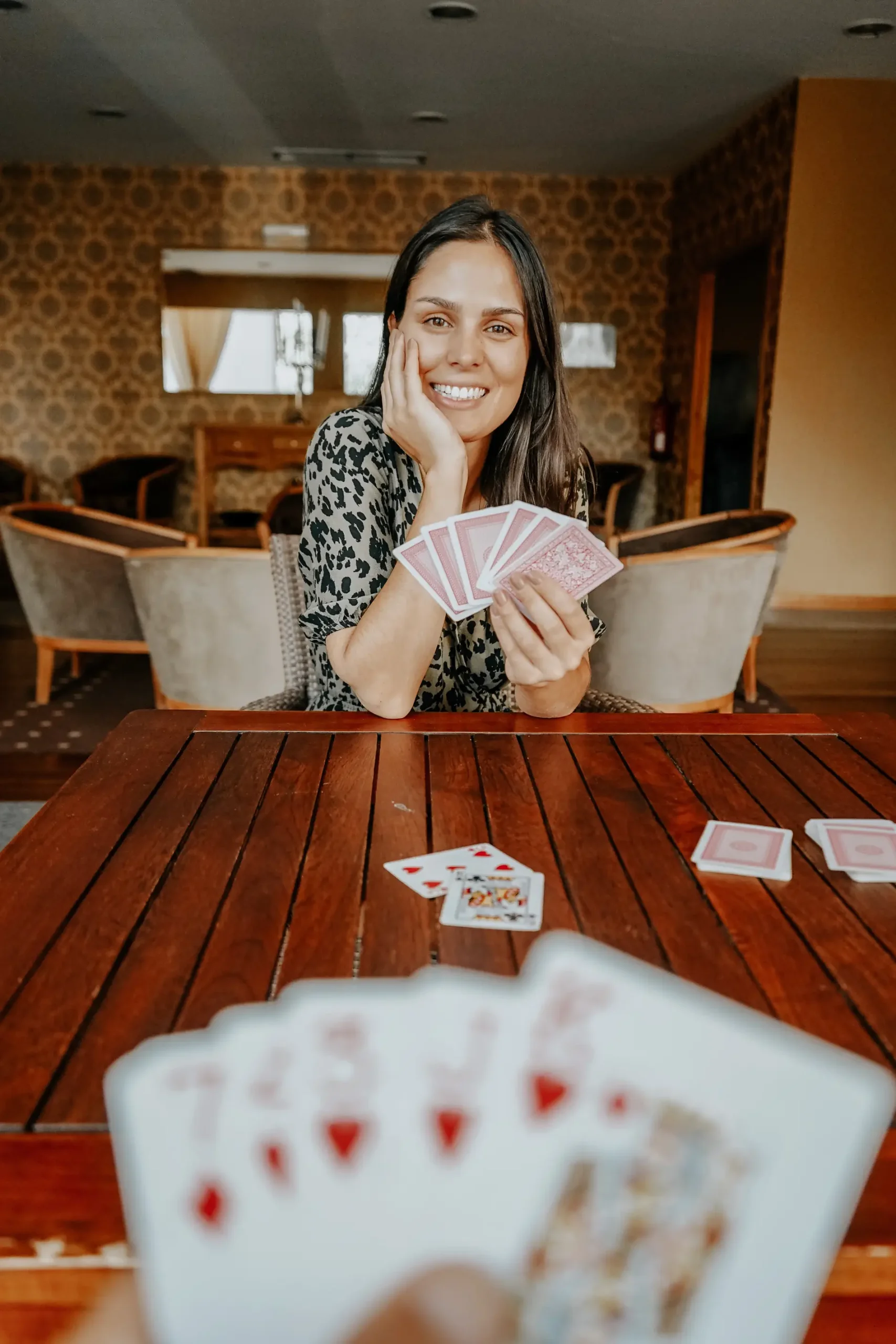Mulher sorridente fazendo truque de cartas, segurando baralho na mesa