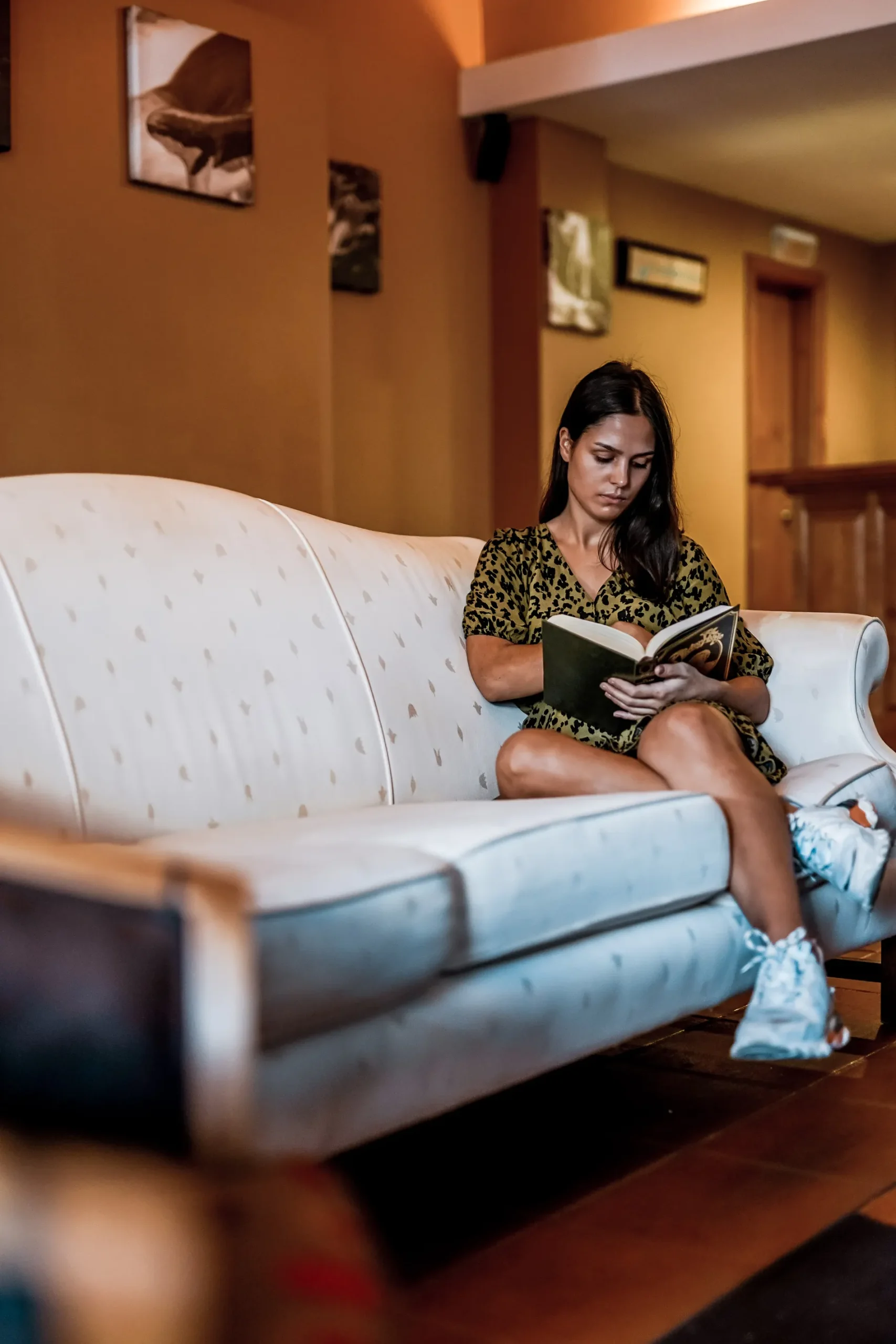 Mulher sentada no sofá lendo um livro em sala aconchegante