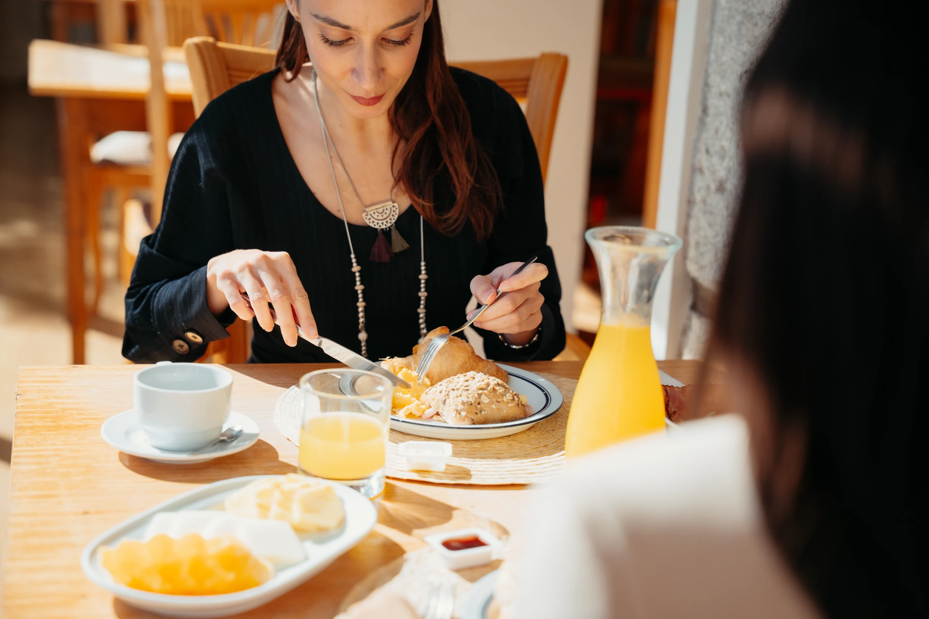 Mulher tomando café da manhã, cortando pão em restaurante com suco de laranja