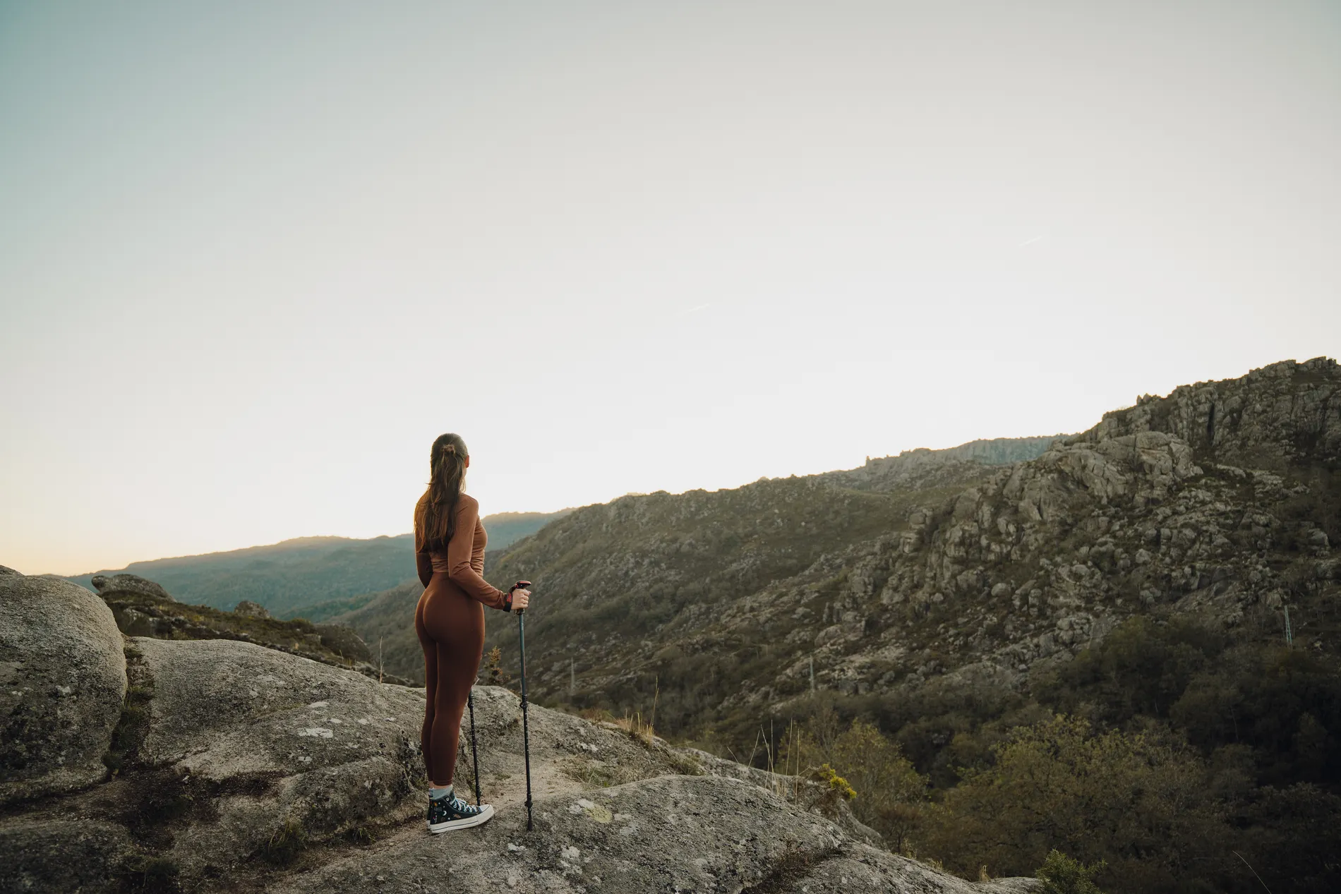 Mulher caminhando nas montanhas, ao pôr do sol, com bastões.