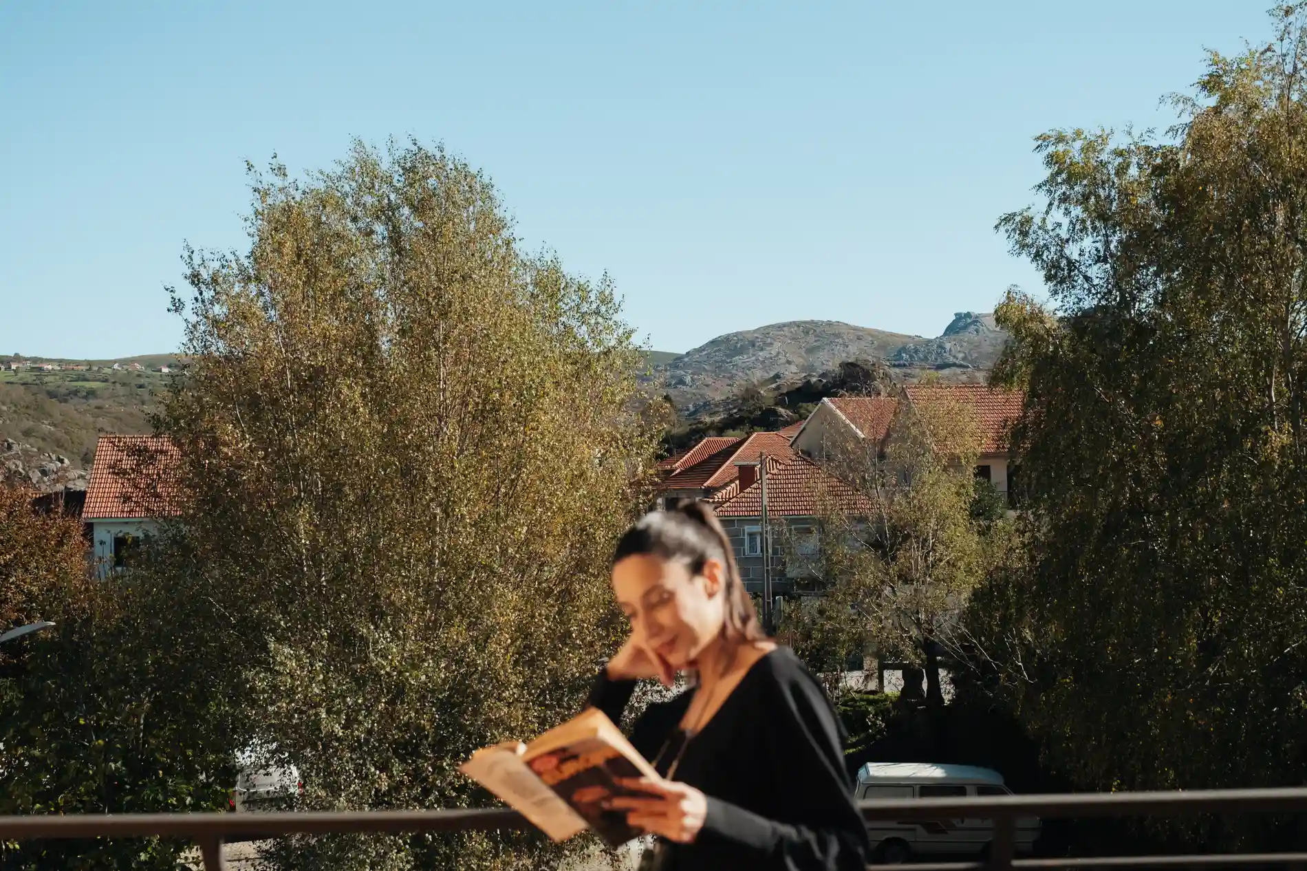 Pessoa lendo livro, árvores e casas com montanha ao fundo