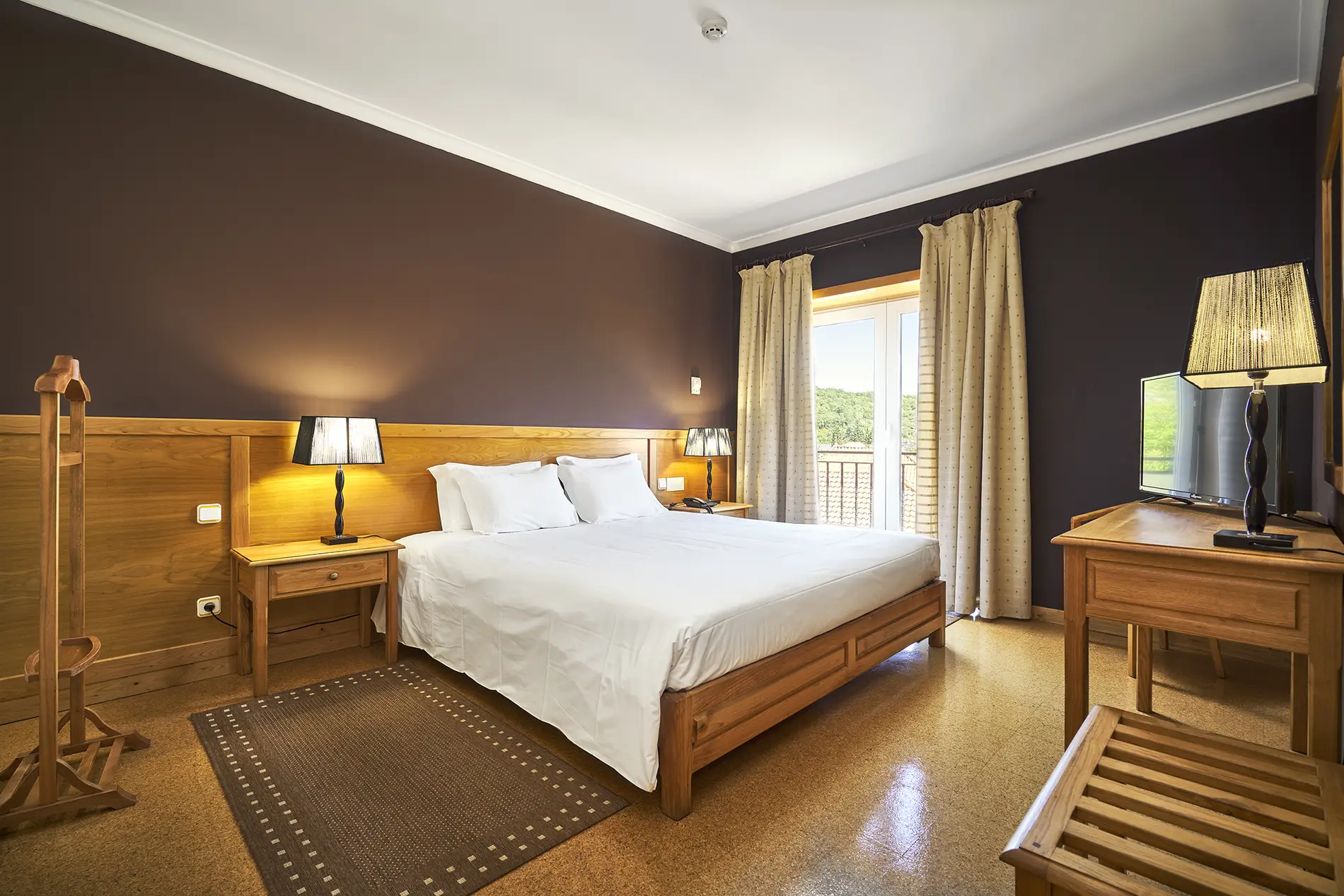 Quarto com cama de casal, cortinas claras e lumin&aacute;rias &agrave; cabeceira.