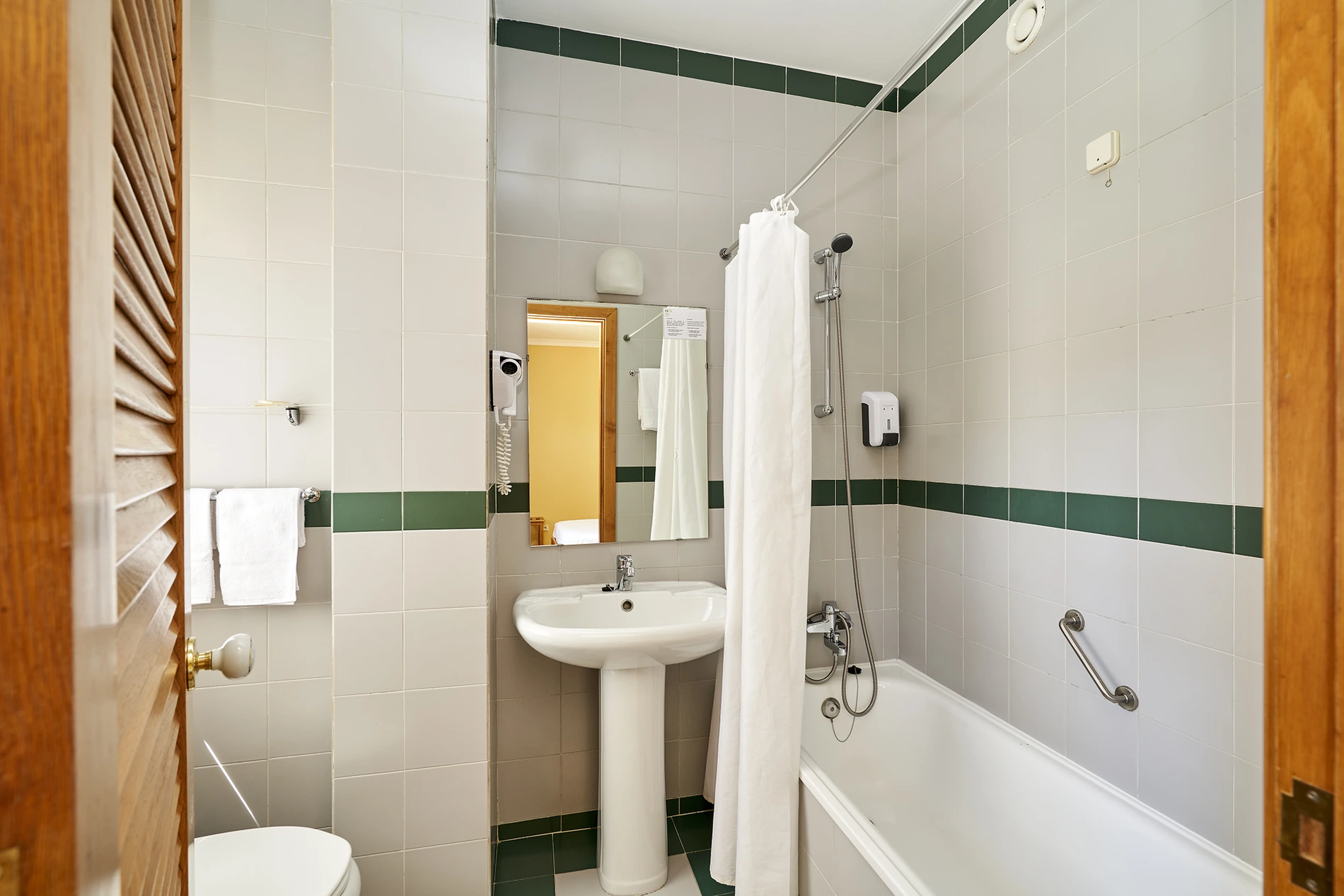 Banheiro moderno com banheira, chuveiro e lavatório, em azulejos claros.