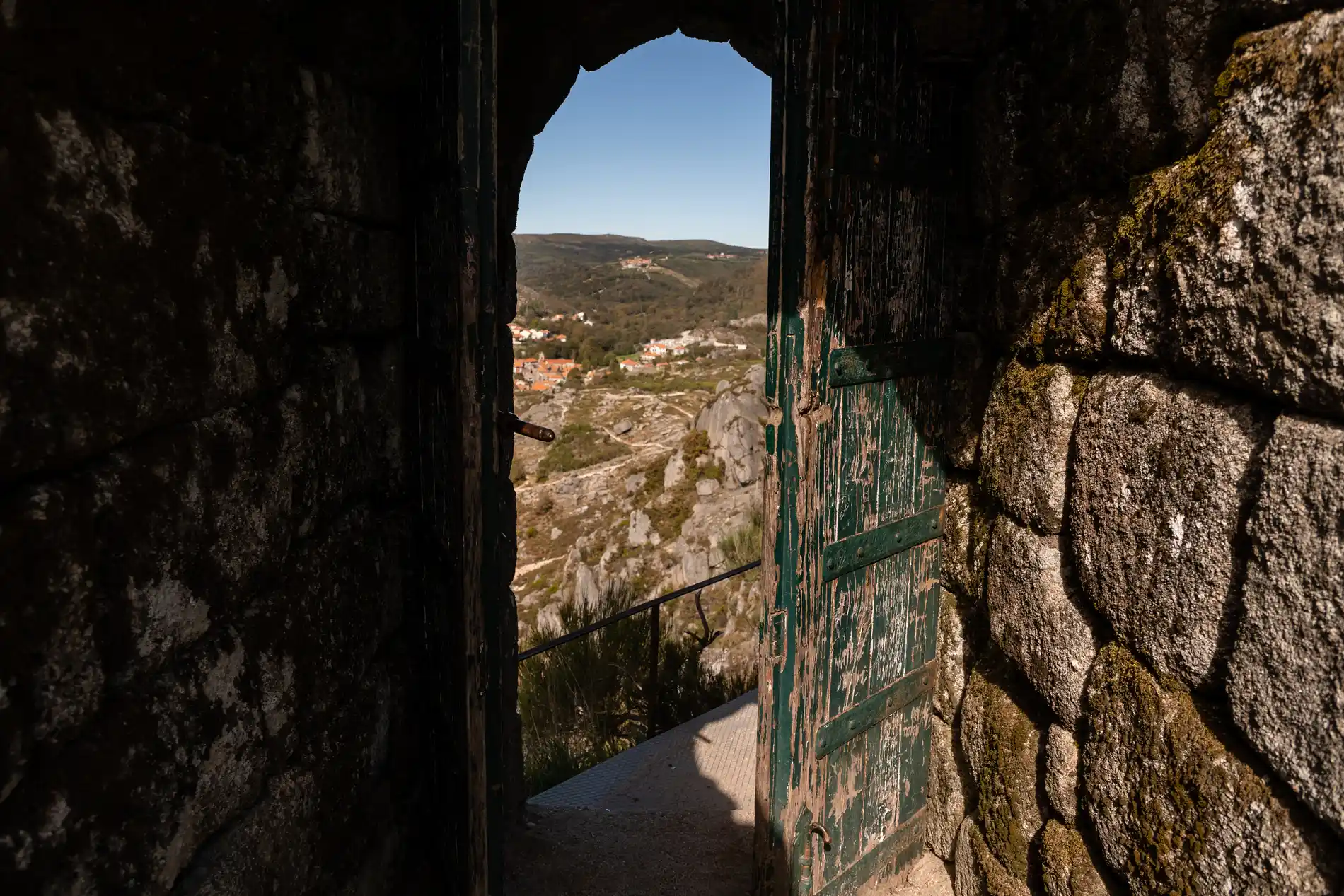 Vista de uma paisagem montanhosa através de arco de pedra e portão verde