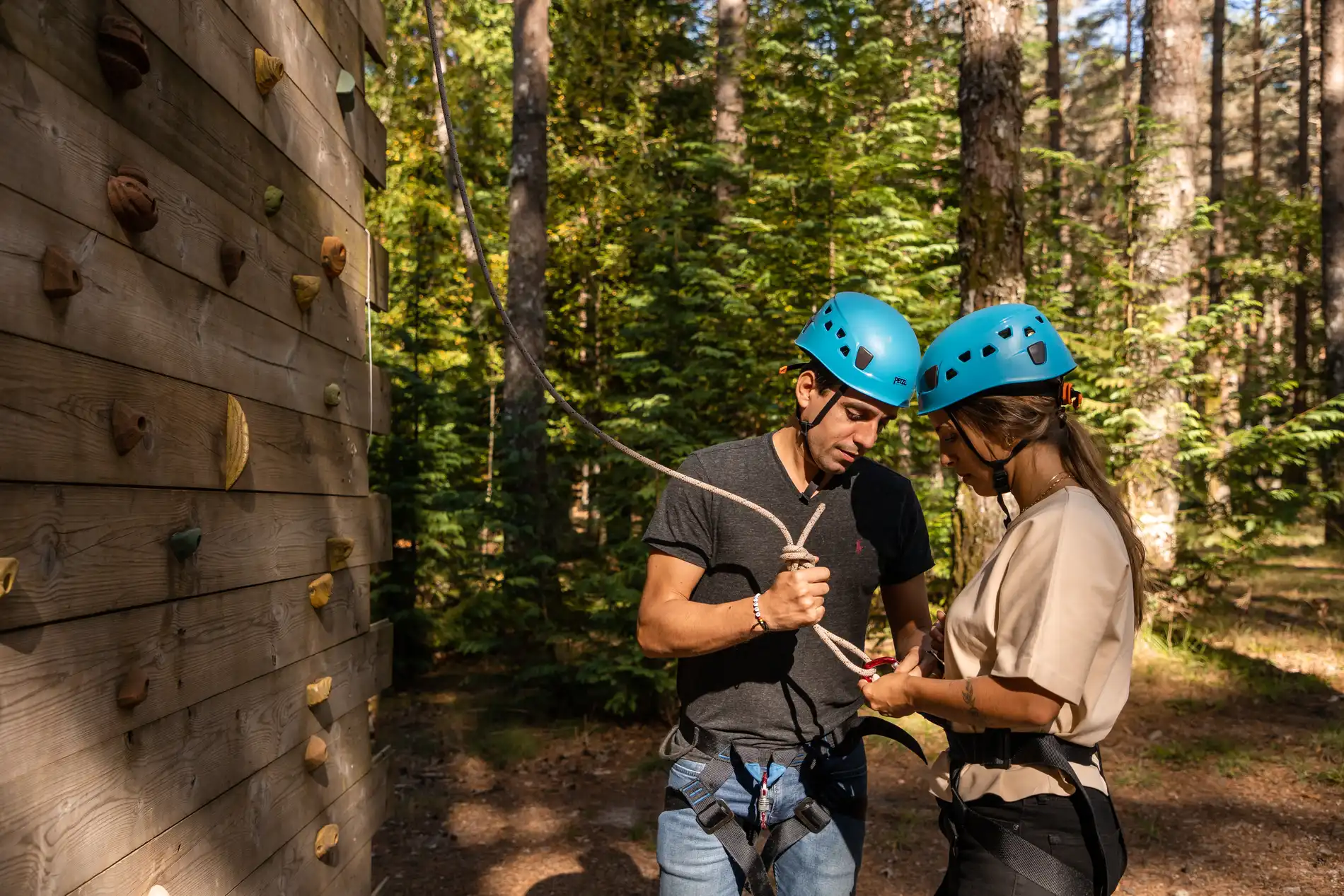 Instrutor e turista com capacete azul em tirolesa no bosque, ajustando corda