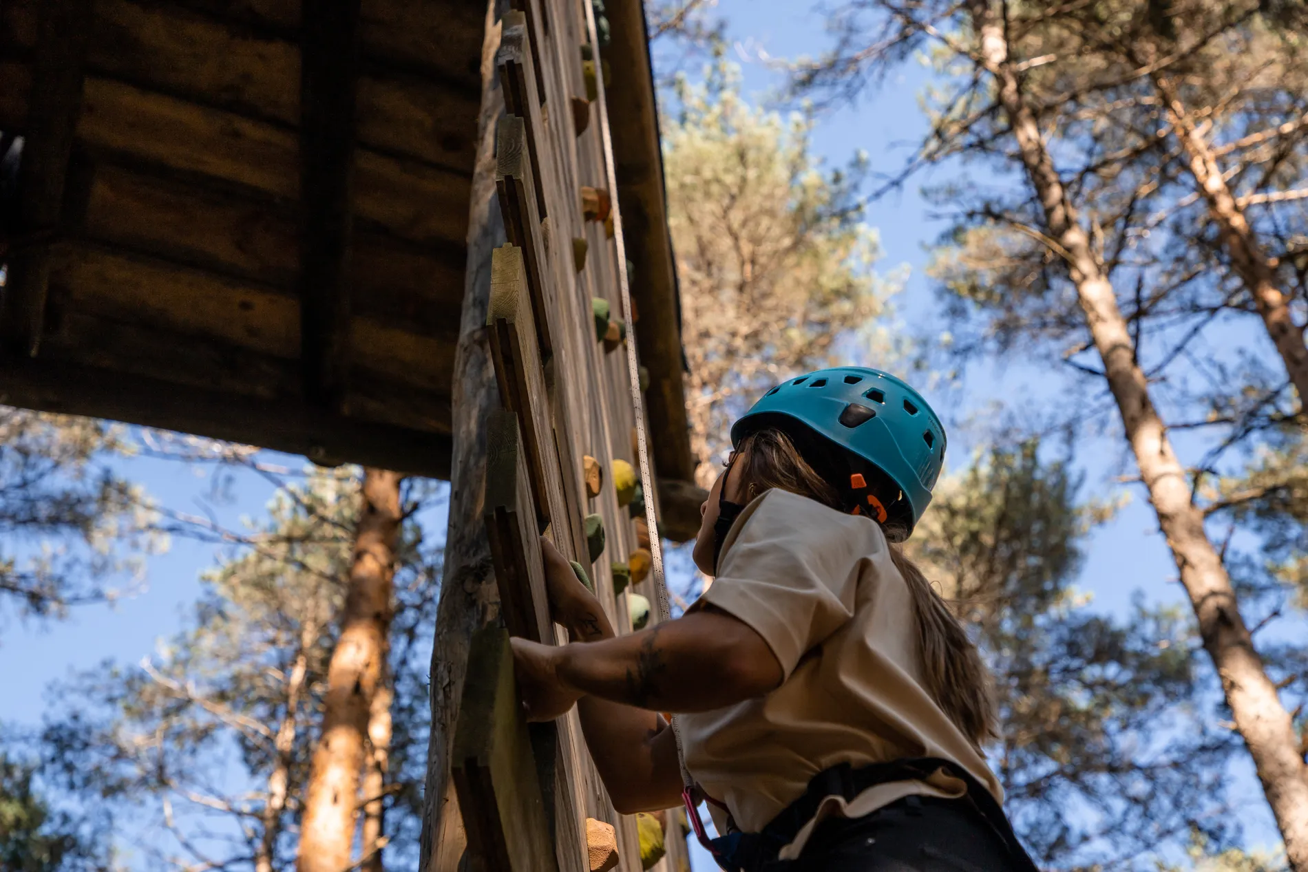 Criança com capacete segura estrutura de escalada ao ar livre, entre árvores