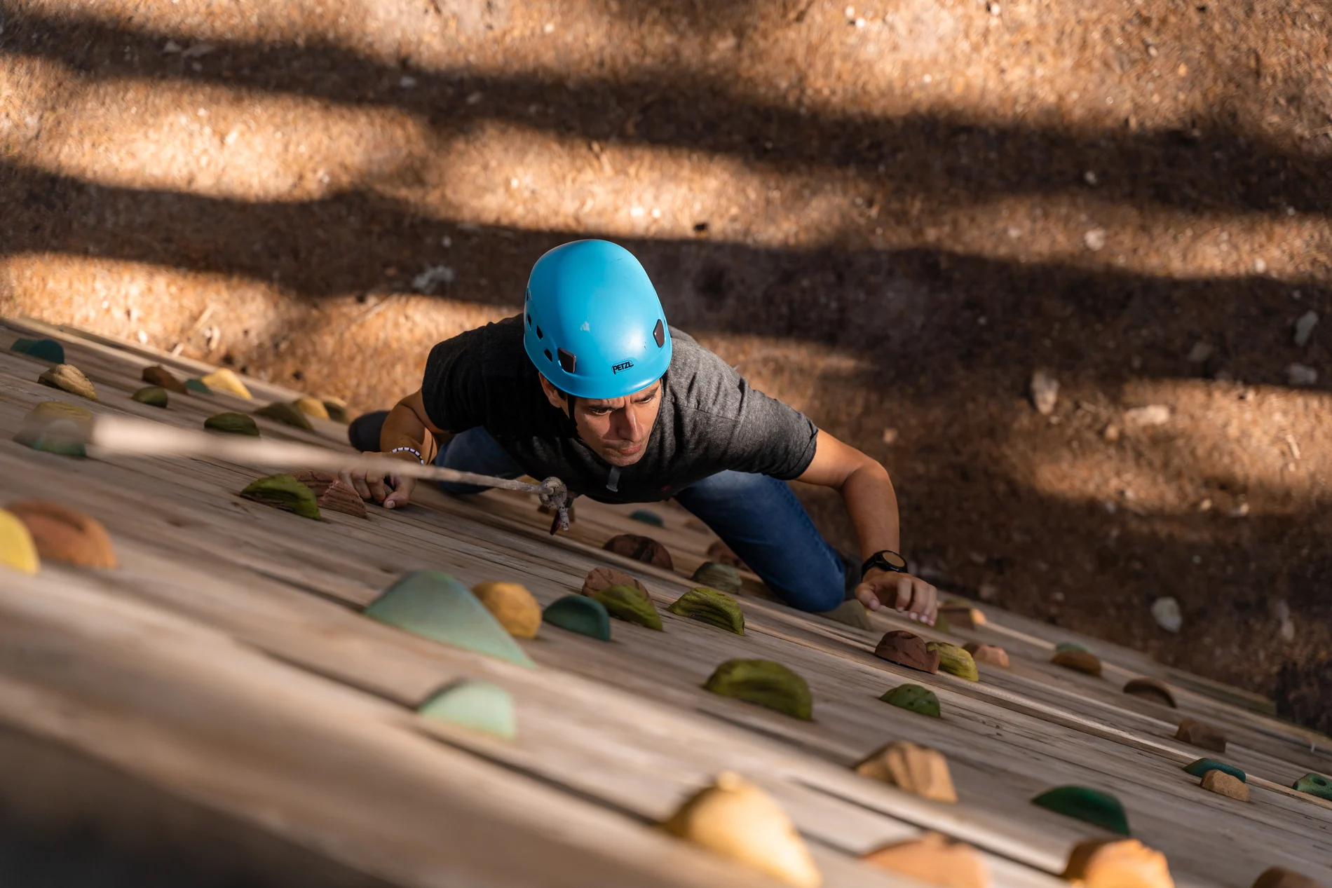 Escalador em capacete azul, fazendo escalada em parede de rocha com presas.
