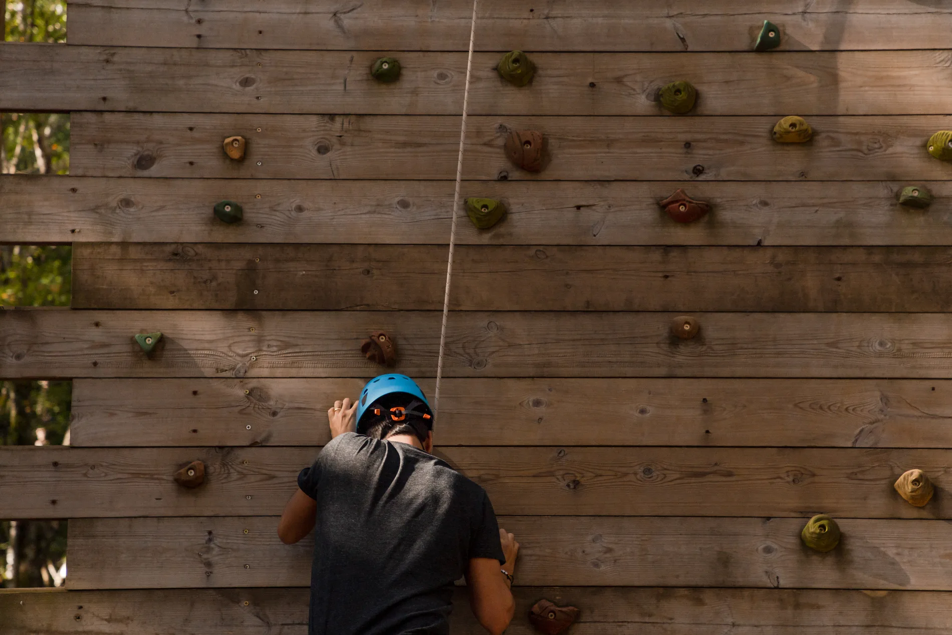 Pessoa com capacete azul escalando em parede de madeira com presas