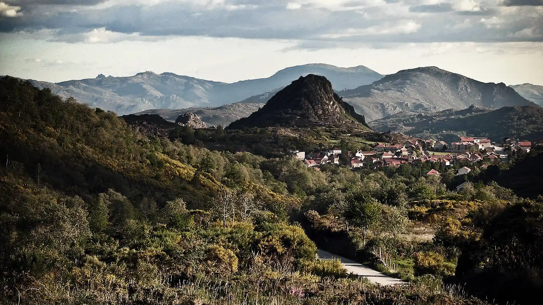 Vale com vila e montanhas ao fundo sob céu nublado