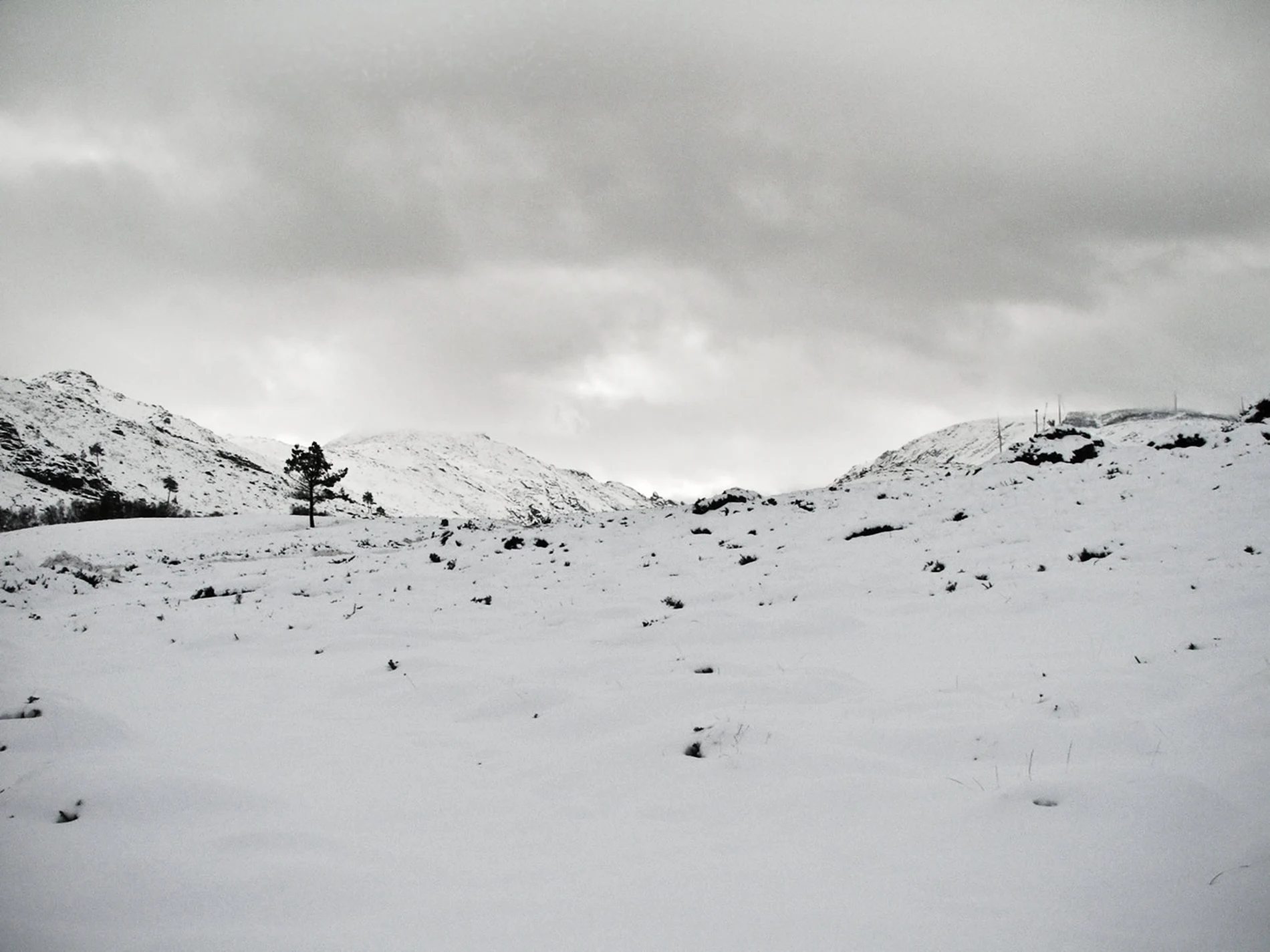 Paisagem montanhosa coberta de neve sob céu nublado, em preto e branco