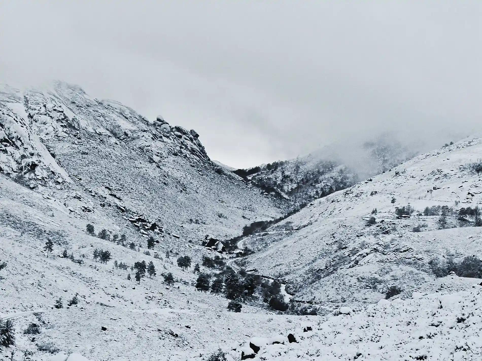 Montanhas nevadas com estrada sinuosa e árvores no vale sob neblina