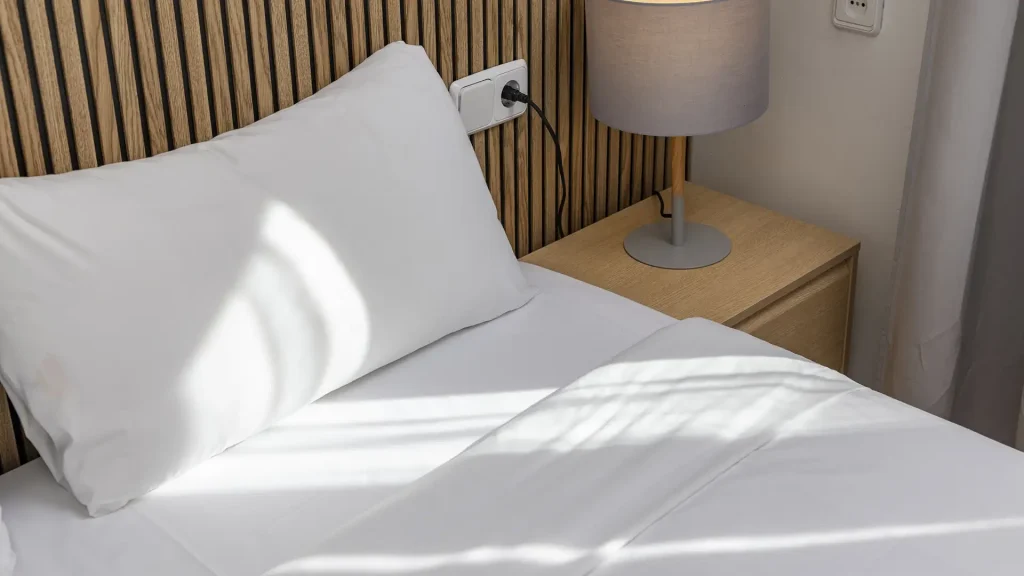 Cama con soporte de l&aacute;mpara y enchufe junto a la cabecera de madera