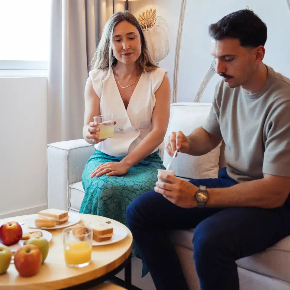 Pareja desayunando en casa, mujer con jugo y hombre comiendo tostadas