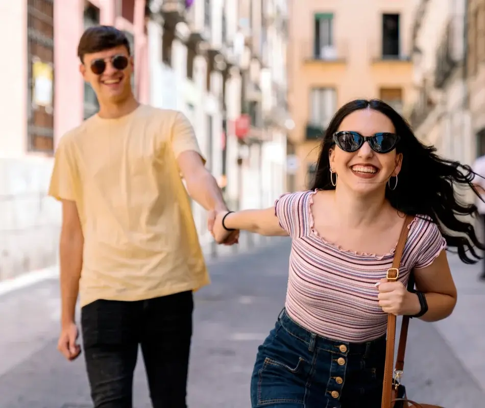 Pareja paseando por la calle, ambos con gafas de sol, sonriendo y caminando