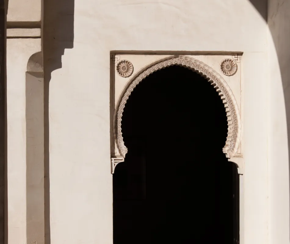Arco de entrada con decoraci&oacute;n tallada, interior oscuro y fachada blanca.