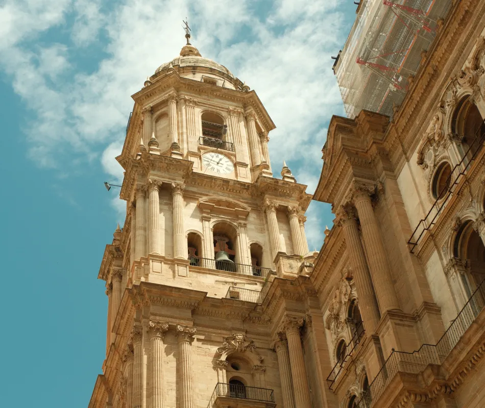 Torre de una catedral barroca con reloj y campanario, vista desde abajo.