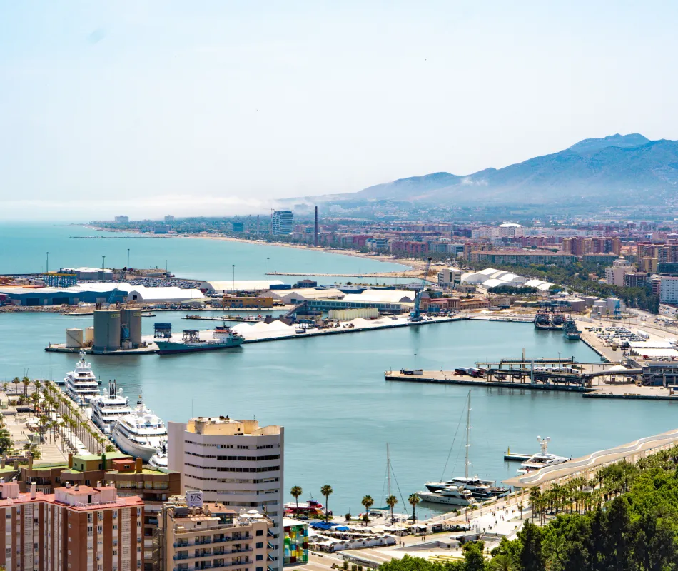 Puerto mar&iacute;timo con yates, edificios costeros y monta&ntilde;as al fondo