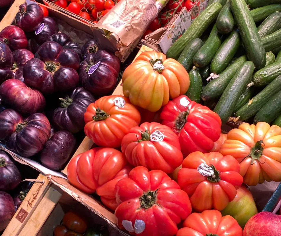 Tomates rojos y naranjas, cebollas moradas y pepinos verdes en un puesto de mercado