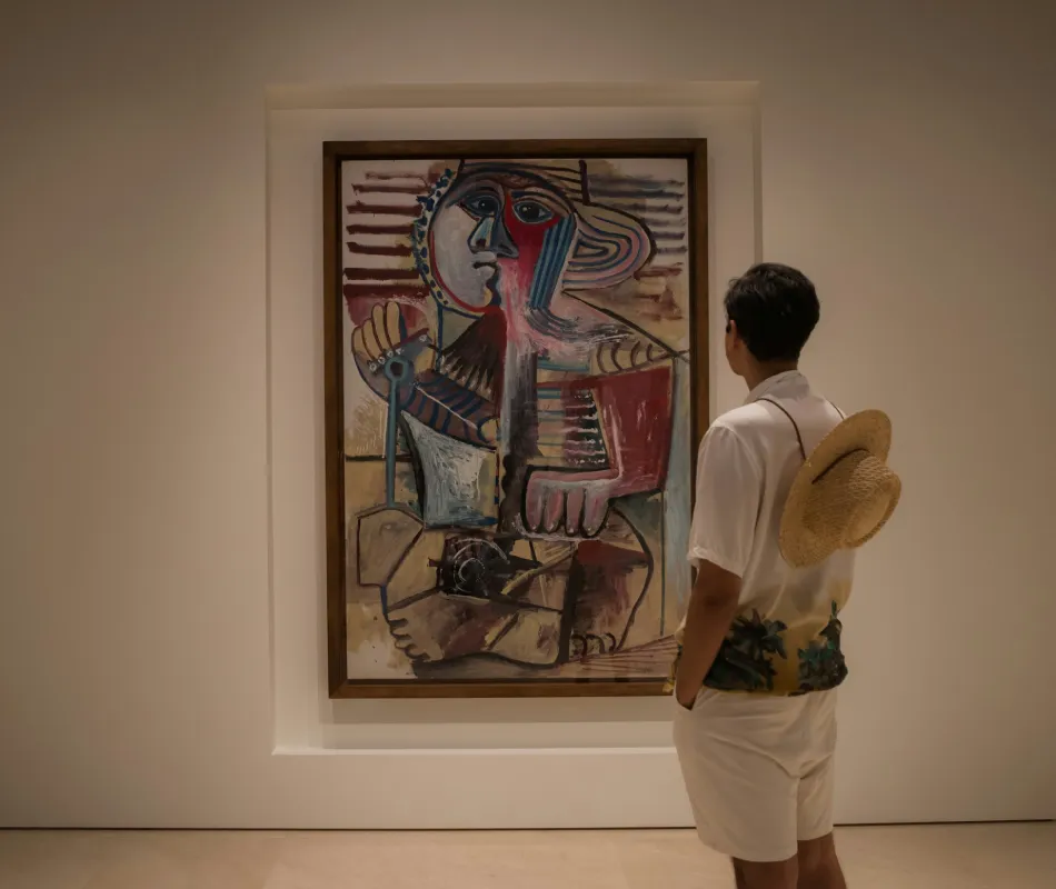 Persona observa un cuadro abstracto de rostro con guitarra en una galer&iacute;a