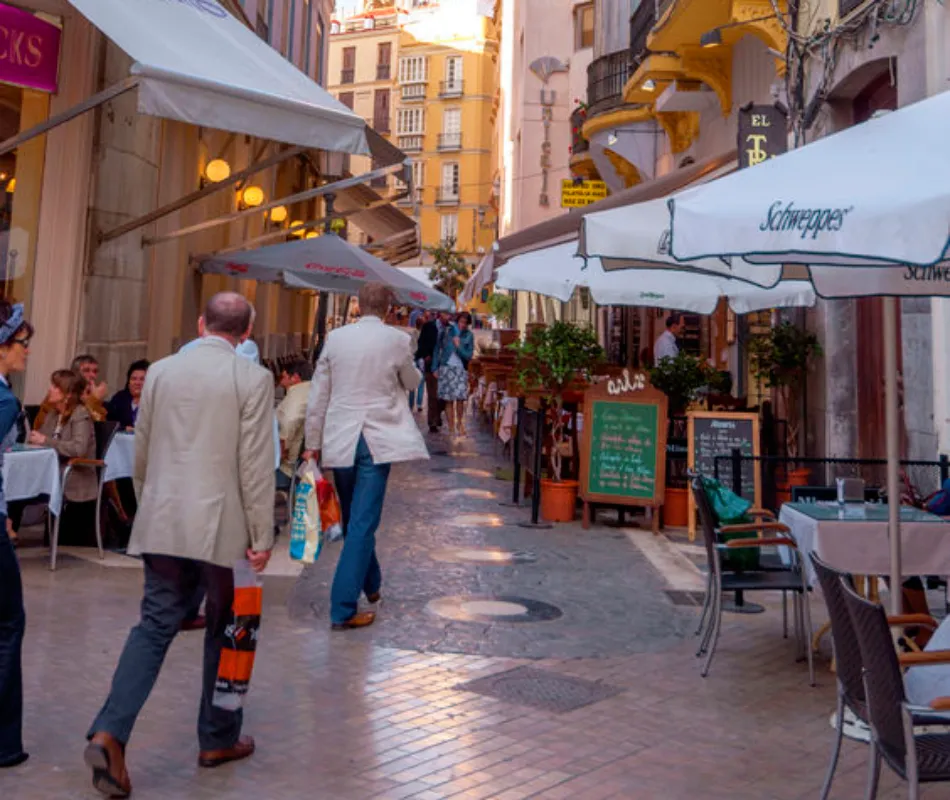 Calle peatonal con terrazas, toldos blancos y gente caminando en Madrid