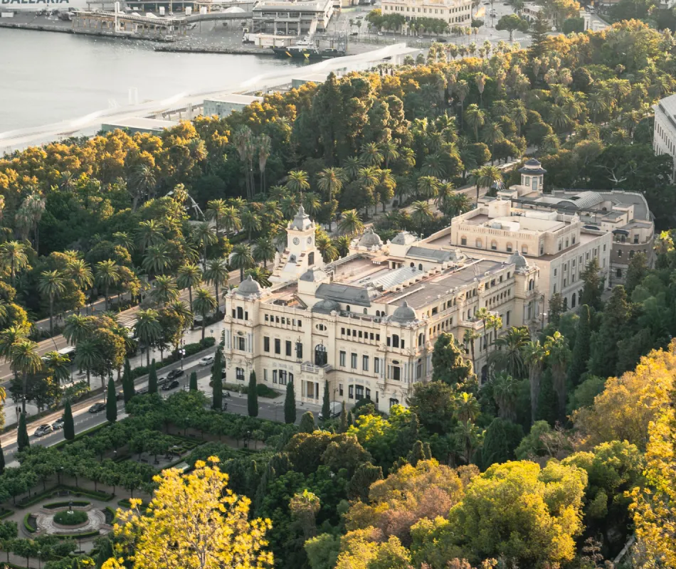 Vista a&eacute;rea de palmeras y jardines junto a un edificio hist&oacute;rico junto al r&iacute;o
