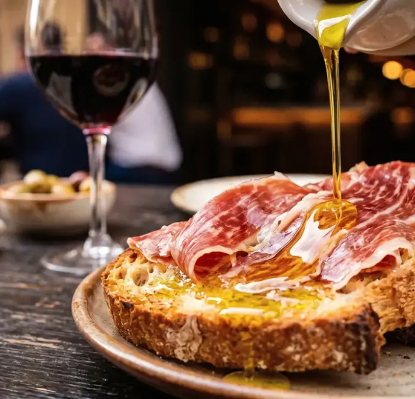 Rebanada de jam&oacute;n ib&eacute;rico con aceite dorado cayendo, fondo con vino.