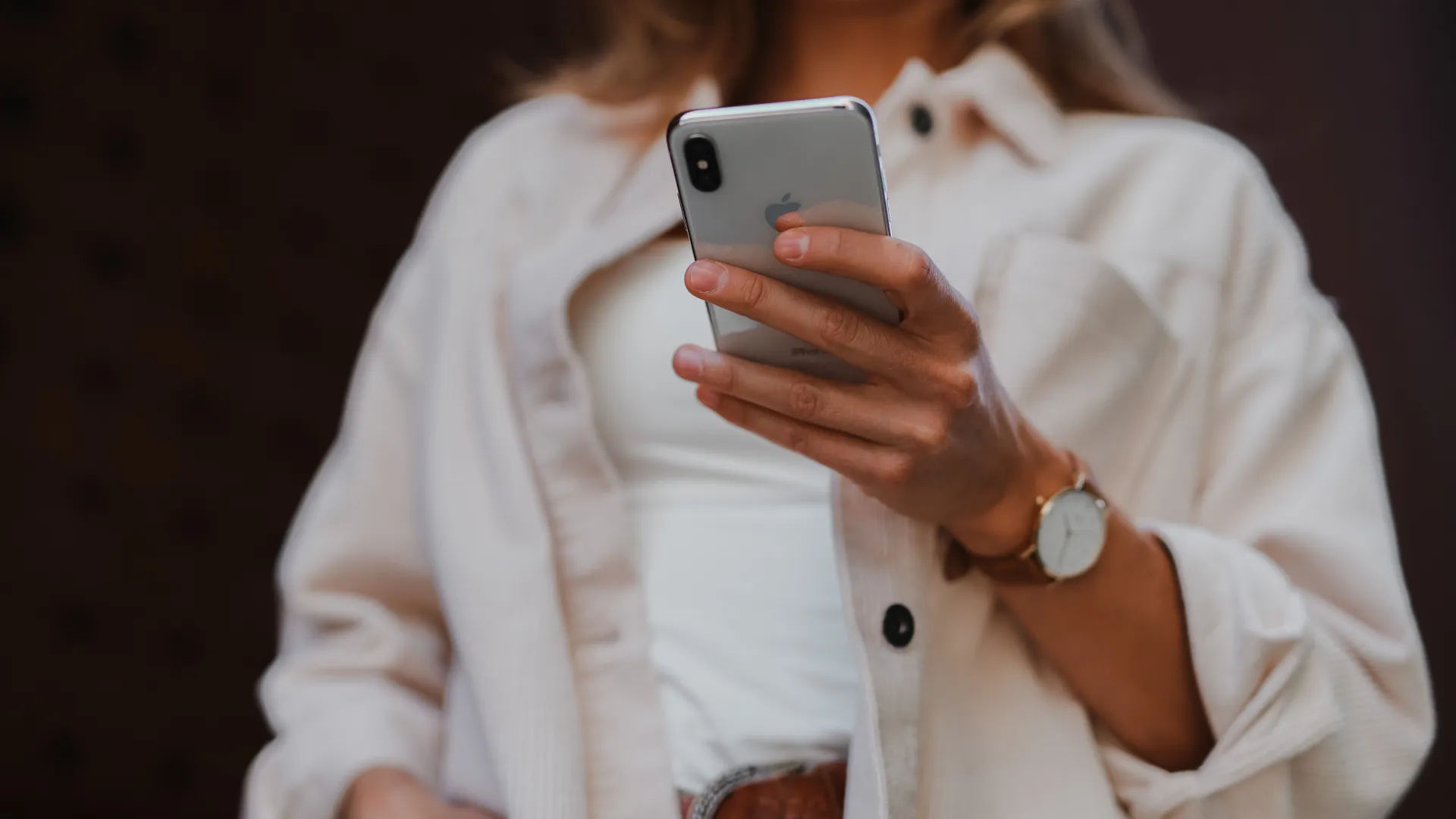 Persona con celular iPhone en mano, con camisa blanca y reloj