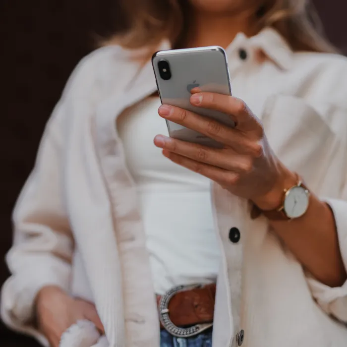 Persona con camisa blanca usando un tel&eacute;fono m&oacute;vil gris.
