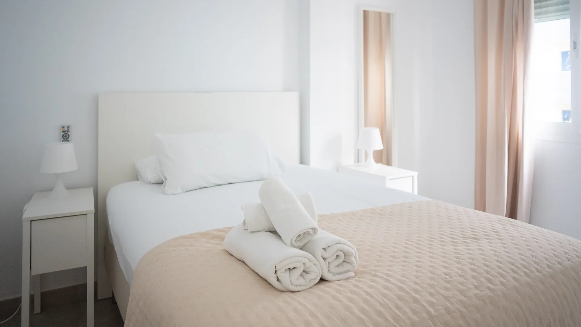 Dormitorio blanco con cama, cojines y mantas dobladas, luz natural