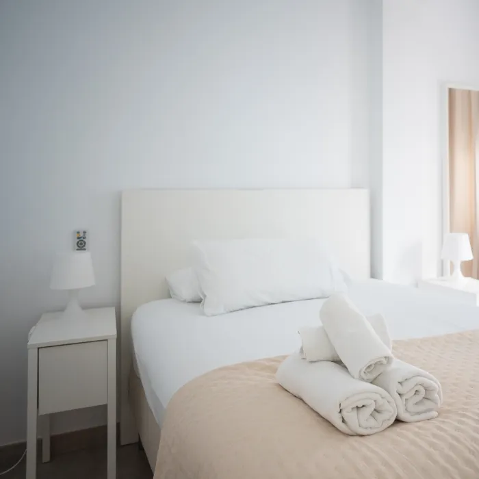 Dormitorio moderno con cama blanca y l&aacute;mparas, s&aacute;banas dobladas.