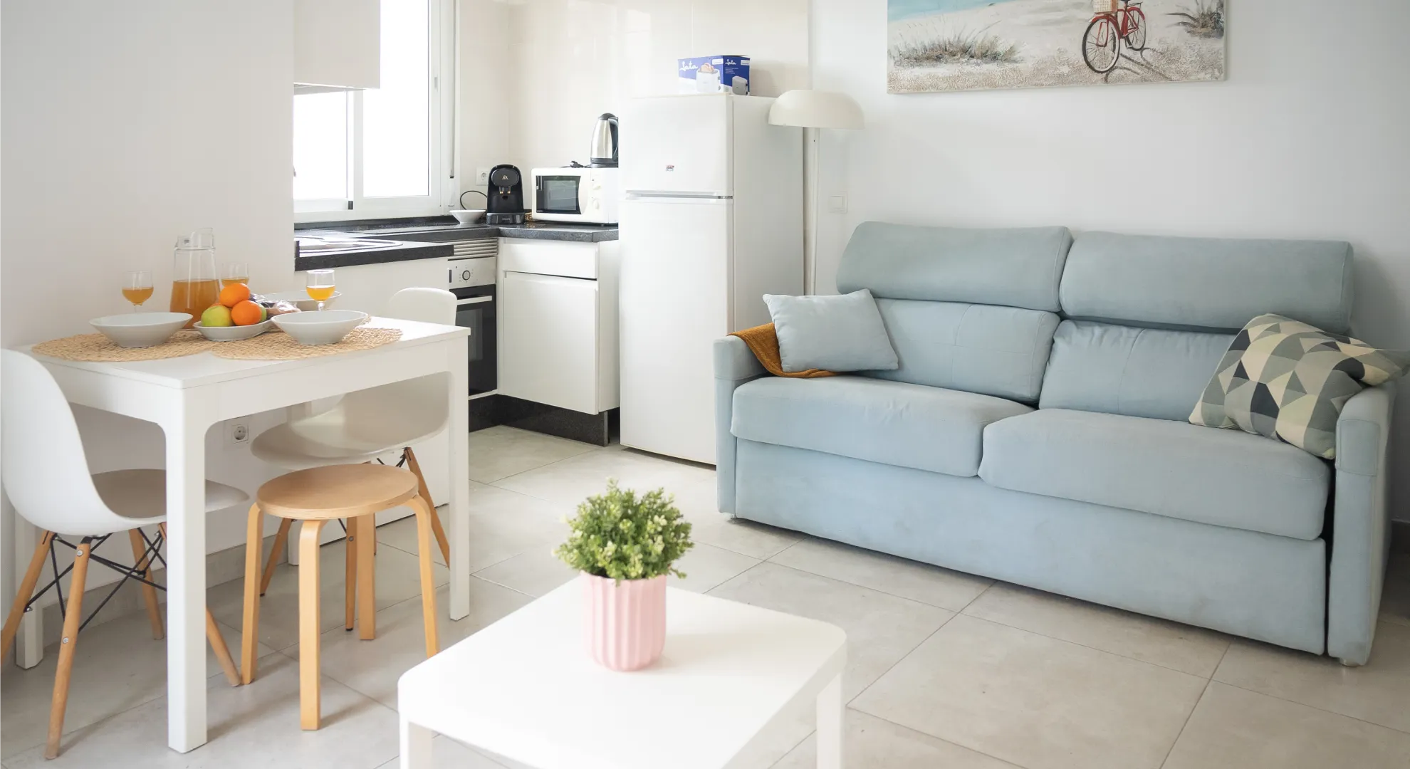 Sala moderna con sof&aacute; azul, mesa blanca y cocina integrada con cafetera