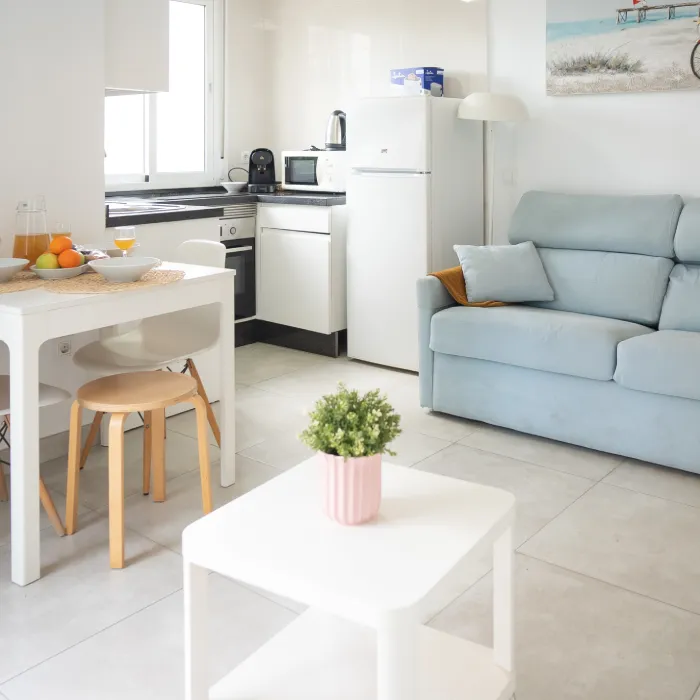 Cocina y sala modernas con sof&aacute; azul y mesa blanca en el centro.