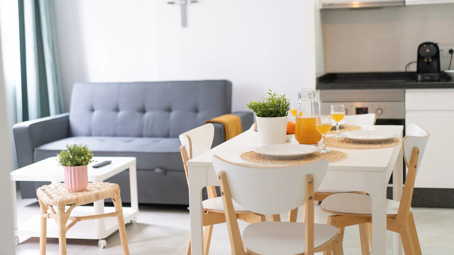 Mesa de comedor con vasos y jugo, sala luminosa con sof&aacute; gris