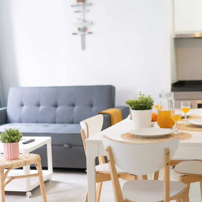 Mesa de comedor con zumo y plantas en sala luminosa con sof&aacute; gris